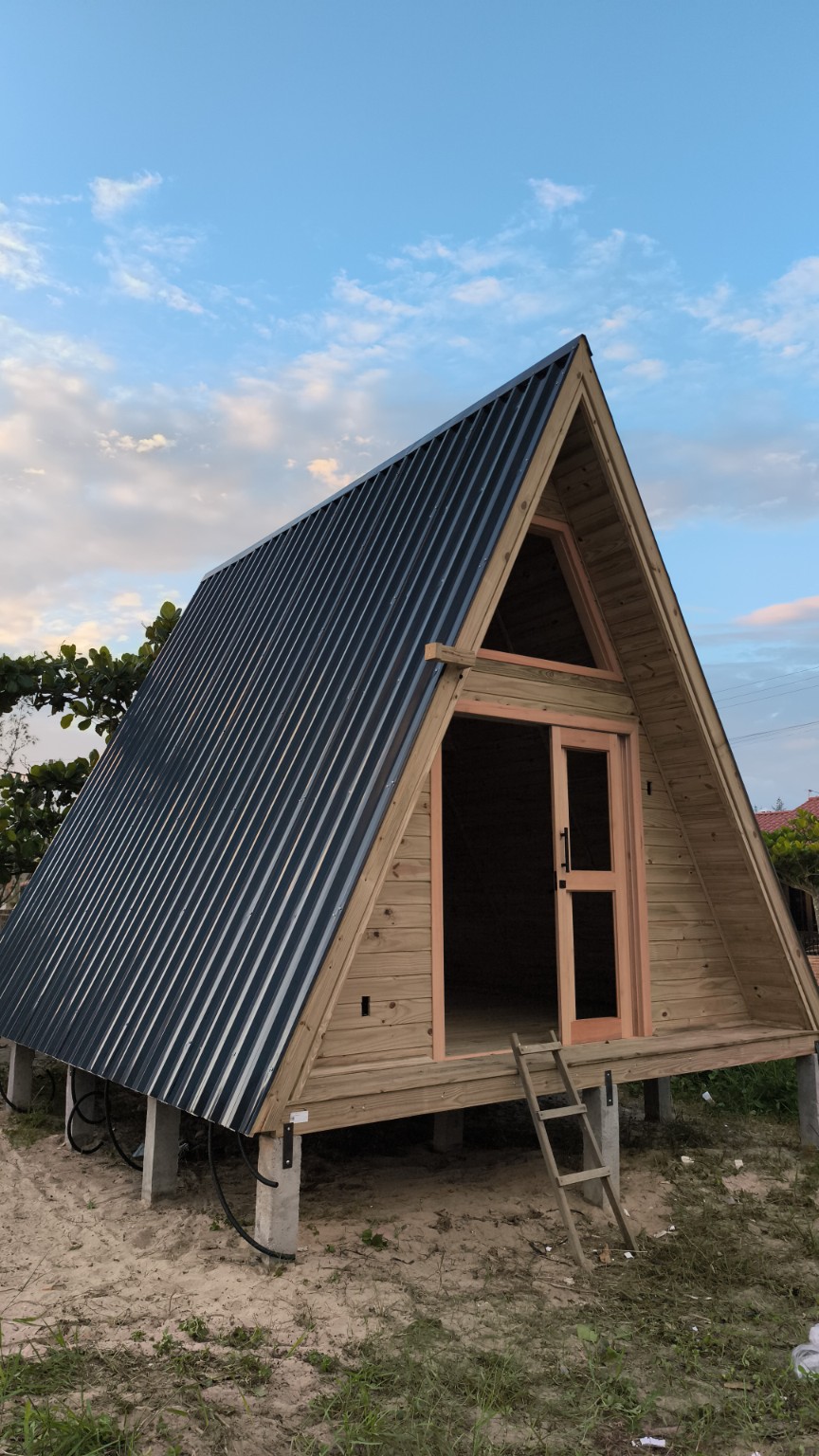Fachada de chalé A-frame de madeira com telhado metálico escuro em Tubarão