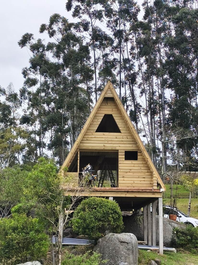 Chalé A-frame em madeira em construção entre eucaliptos
